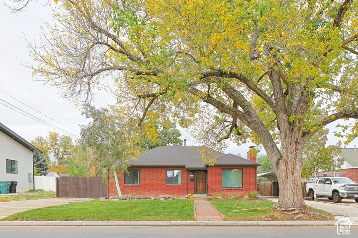 Red brick exterior featuring a multi-hipped roofline, prominent masonry chimney, brick walkway, and mature landscape trees