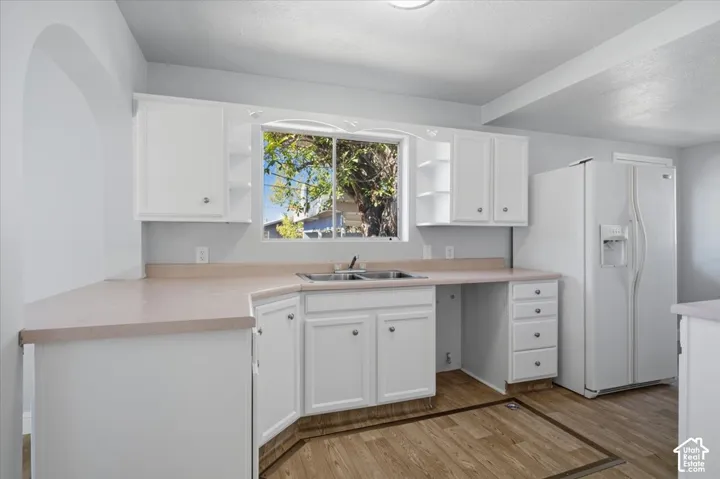 Kitchen featuring white cabinetry with open shelving, laminate countertops, a double-basin stainless steel sink, and wood-finish flooring
