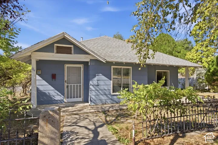 Single-story exterior featuring blue siding, a shingled hipped roof, a covered front porch, and decorative metal perimeter fencing