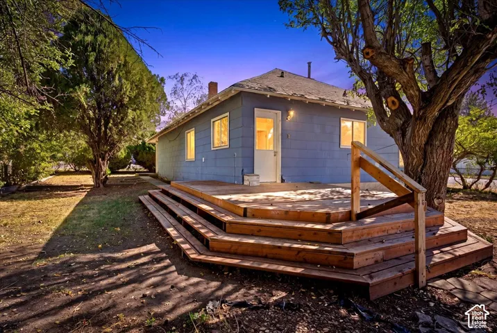 Multi-level wood deck featuring integrated steps and a railing, situated on a lot with mature trees
