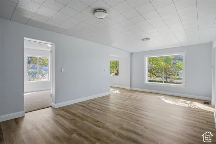 Interior space featuring wood-finish flooring, white grid-patterned ceiling panels, large picture windows, and dual flush-mount ceiling light fixtures