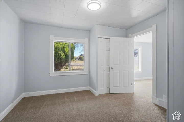 Neutral-toned room featuring carpeted flooring, a flush-mount ceiling fixture, a window with white trim, and a built-in closet with paneled doors