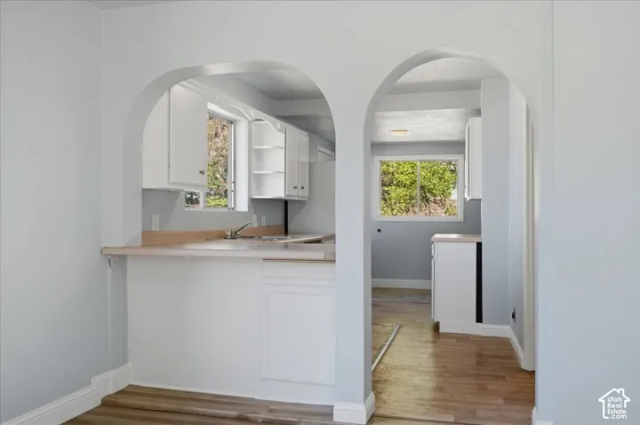 Dual arched doorways, white cabinetry, neutral-toned countertops, and wood-finish flooring