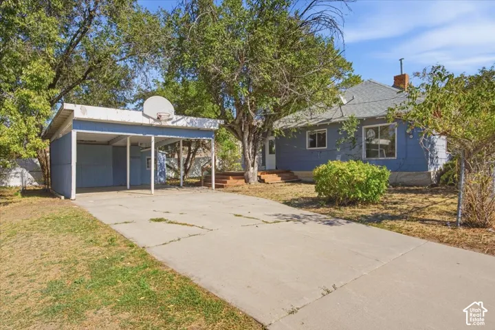 Blue-sided exterior featuring a concrete driveway, detached carport, and mature landscaping