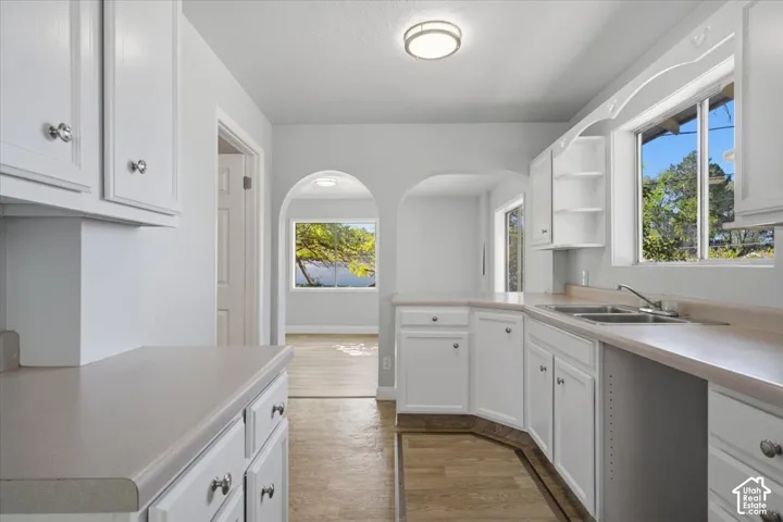 Kitchen featuring white shaker-style cabinetry, solid-surface countertops, dual-basin stainless steel sink, and decorative architectural archways