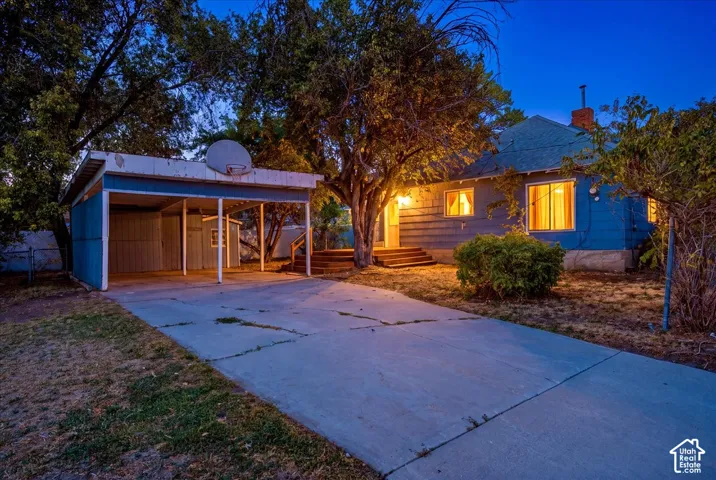 Single-story exterior featuring blue siding, a concrete driveway, a covered carport, and wood-stepped entry