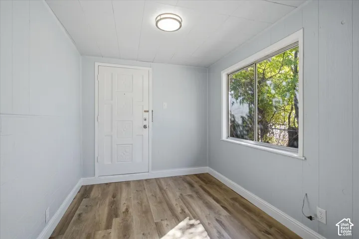 Interior space featuring wood-finish flooring, panelled walls, a single-panel entry door with decorative moulding, a sliding window, and a ceiling-mounted flush light fixture