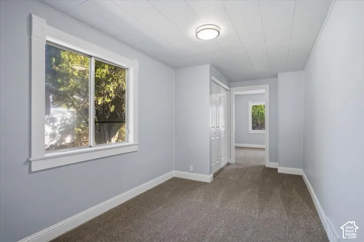 Neutral-toned room featuring wall-to-wall carpeting, a dual-pane sliding window with decorative molding, a ceiling-mounted flush light fixture, and a built-in closet with bi-fold doors