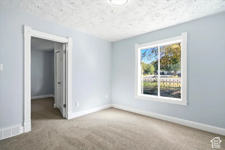 Neutral-toned carpet, textured ceiling, large sliding window with white trim, and architectural door casing