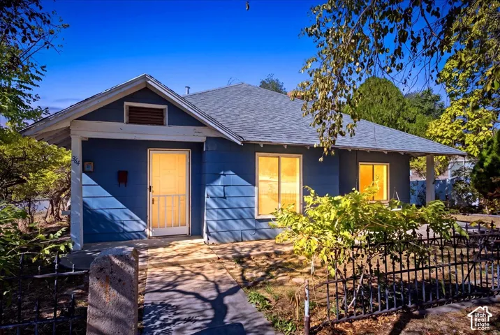 Exterior featuring blue horizontal siding, a hipped roof, a concrete walkway, and metal perimeter fencing