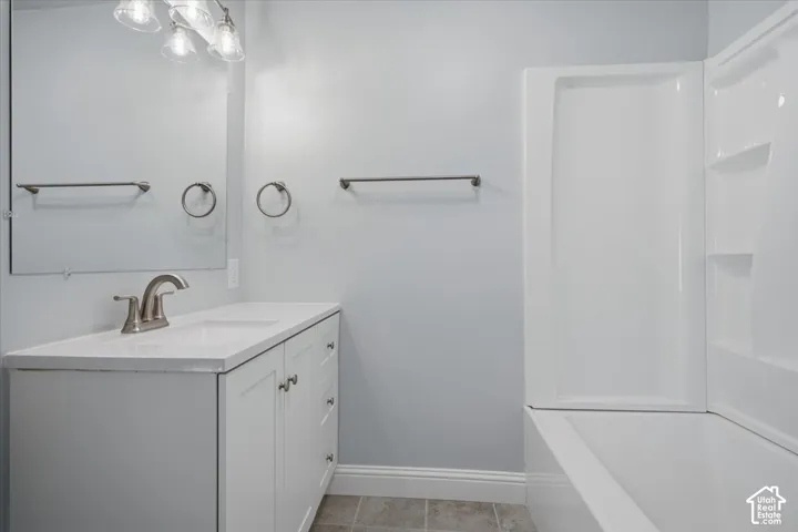 Bathroom featuring white cabinetry, solid-surface countertop with integrated sink, brushed-nickel faucet, and a white tub-shower combination