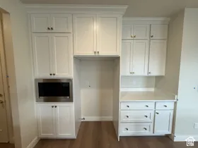 Custom white cabinetry with shaker-style doors, built-in microwave, stone-surface countertop, and wood-finish flooring