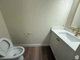 White vanity with a solid surface countertop, undermount sink, gold-toned faucet, and wood-finish flooring