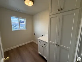 Utility area featuring wood-finish flooring, white shaker-style cabinetry, tall built-in storage, and a white countertop