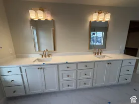 Double vanity featuring white cabinetry, quartz countertop, rectangular undermount sinks, brass-toned fixtures, and wall-mounted vanity lights with glass shades
