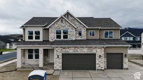 Two-story exterior featuring a stone veneer facade, shingle roof, multi-pane windows, and a three-car garage
