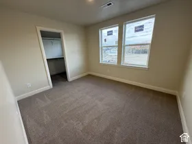 Neutral-toned interior featuring wall-to-wall carpeting, dual windows providing natural illumination, and a built-in closet with shelving