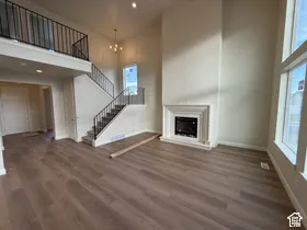 Double-height living area featuring floor-to-ceiling fireplace surround, wood-finish flooring, metal staircase railing, and large windows