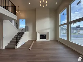 Expansive two-story living area featuring vaulted ceilings, floor-to-ceiling windows, a structured fireplace surround, metal baluster staircase, and wood-finish flooring