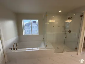 Soaking tub and glass-enclosed shower featuring bronze-finish hardware, built-in shelving, and large-format tile flooring