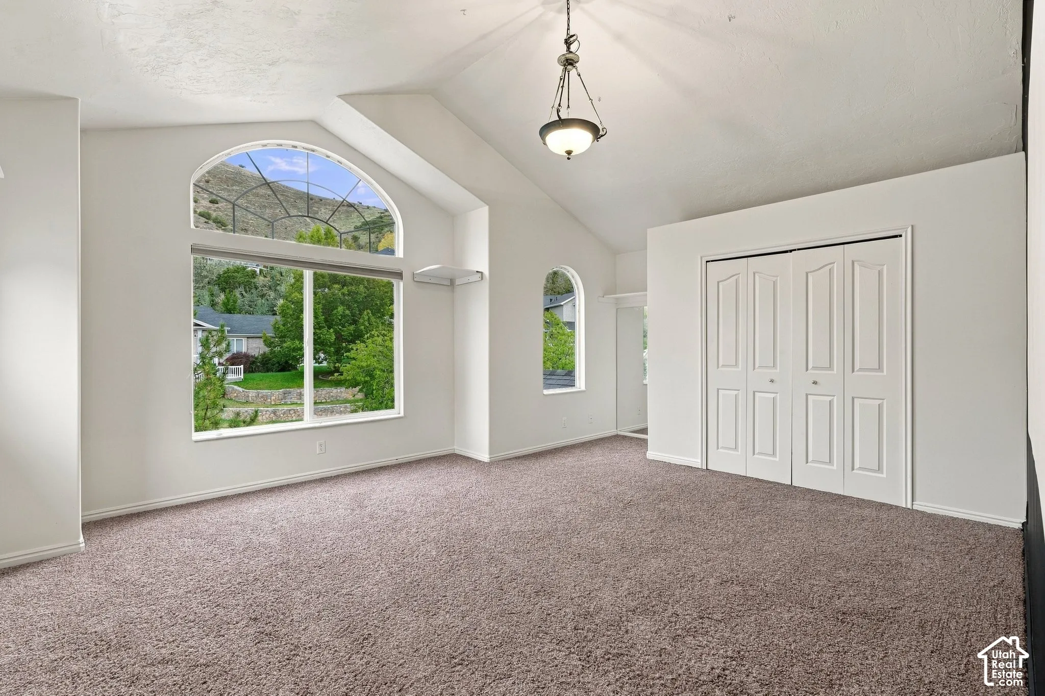 Vaulted ceiling featuring a central pendant light, arch-top windows, and bifold closet doors