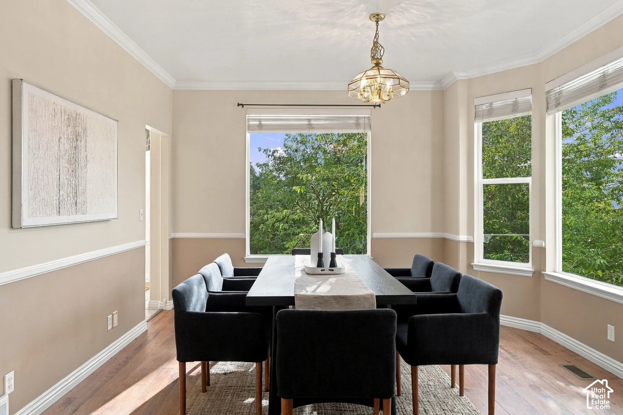 Dining area featuring wood-finish flooring, two-tone wall paint with chair rail molding, crown molding, large windows, and a decorative pendant light fixture