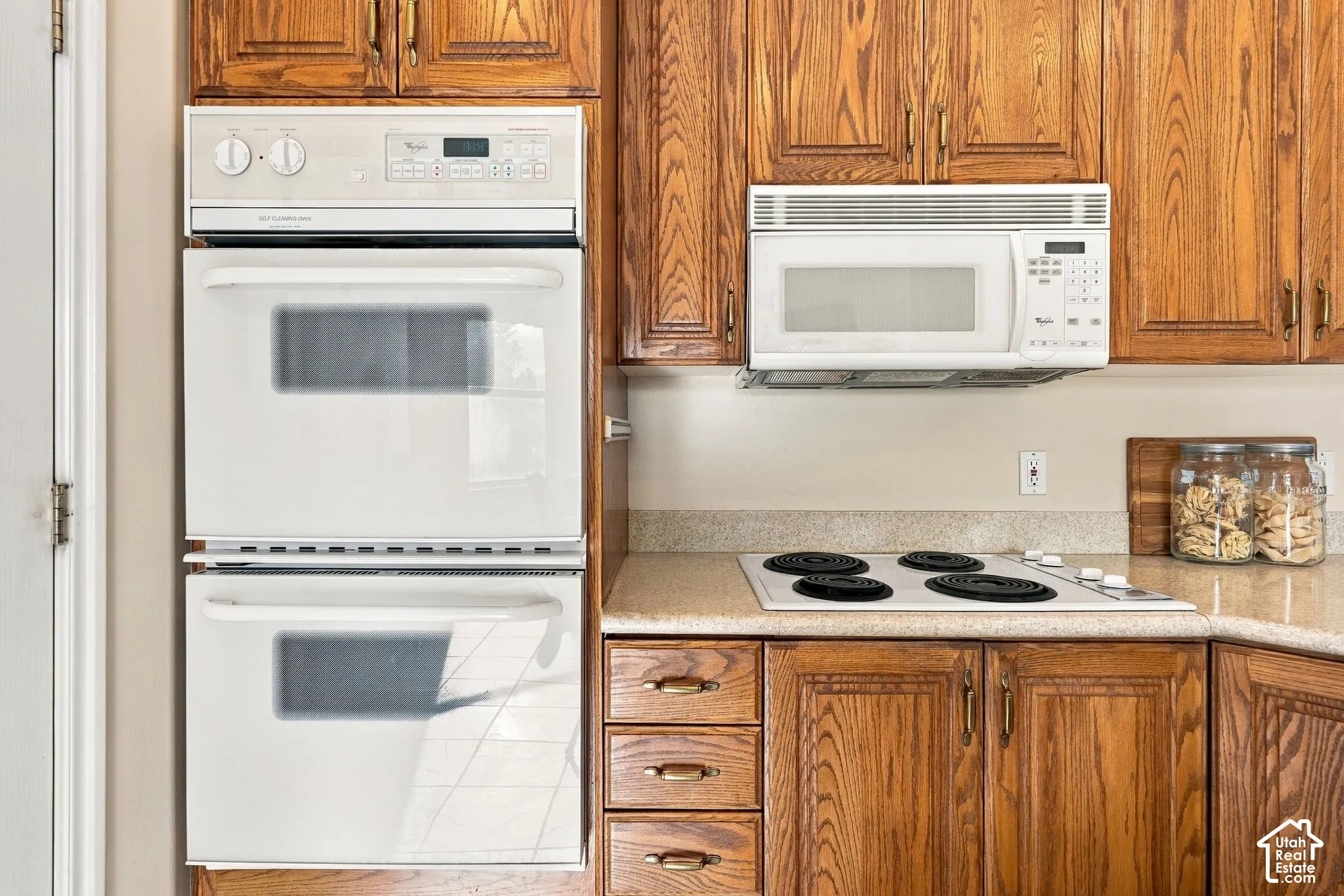 Kitchen featuring natural wood cabinetry, built-in double ovens, over-the-range microwave, electric cooktop, and speckled solid-surface countertops