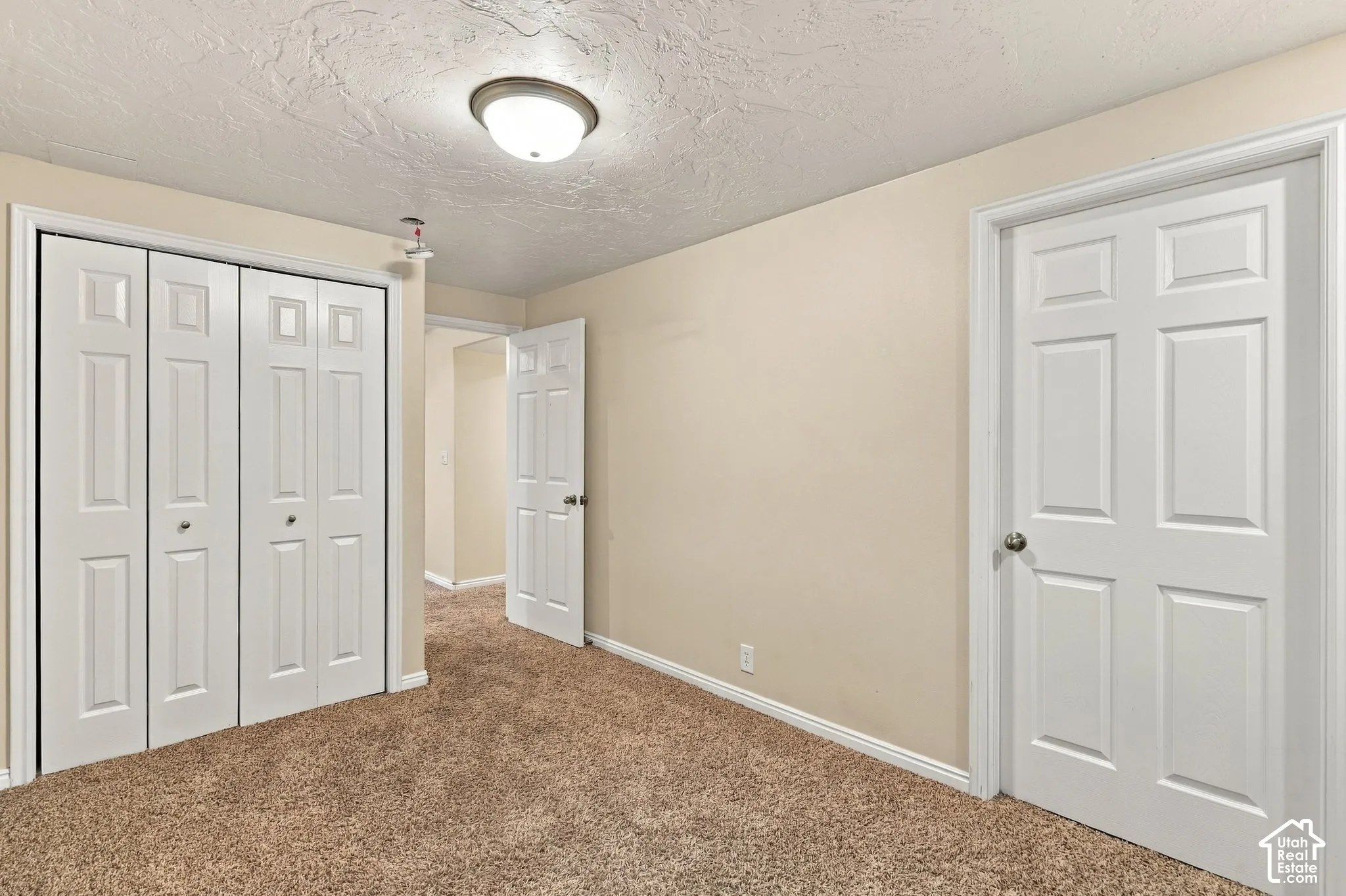 Room featuring wall-to-wall carpeting, textured ceiling, flush-mount lighting, bifold closet doors, and six-panel interior doors