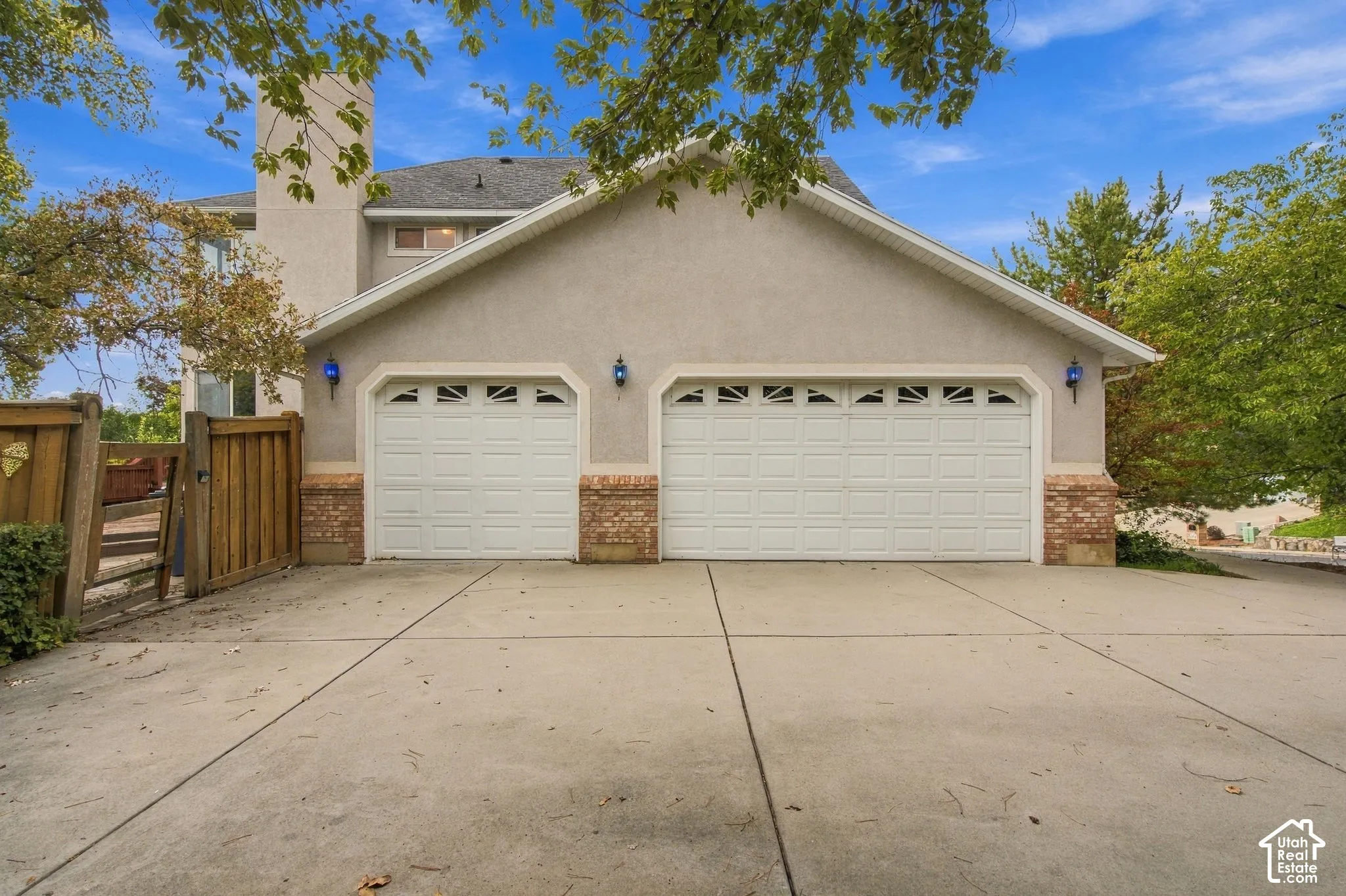 Exterior featuring a two-car garage with paneled doors, stucco siding, brick-accented pillars, and a concrete driveway