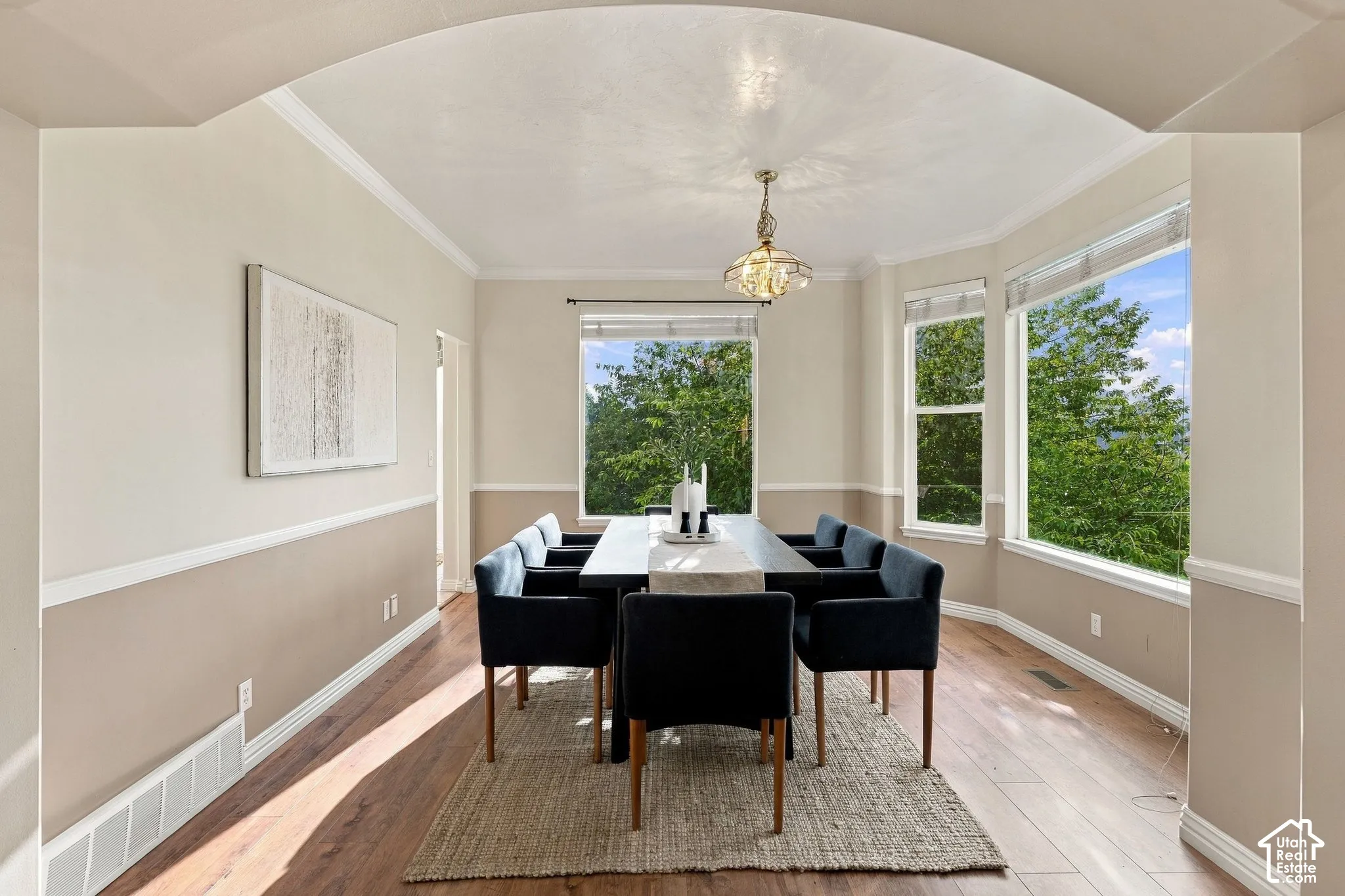 Dining room featuring an arched entryway, wood-finish flooring, two-tone wall paint with chair rail molding, and large windows with greenery exposure