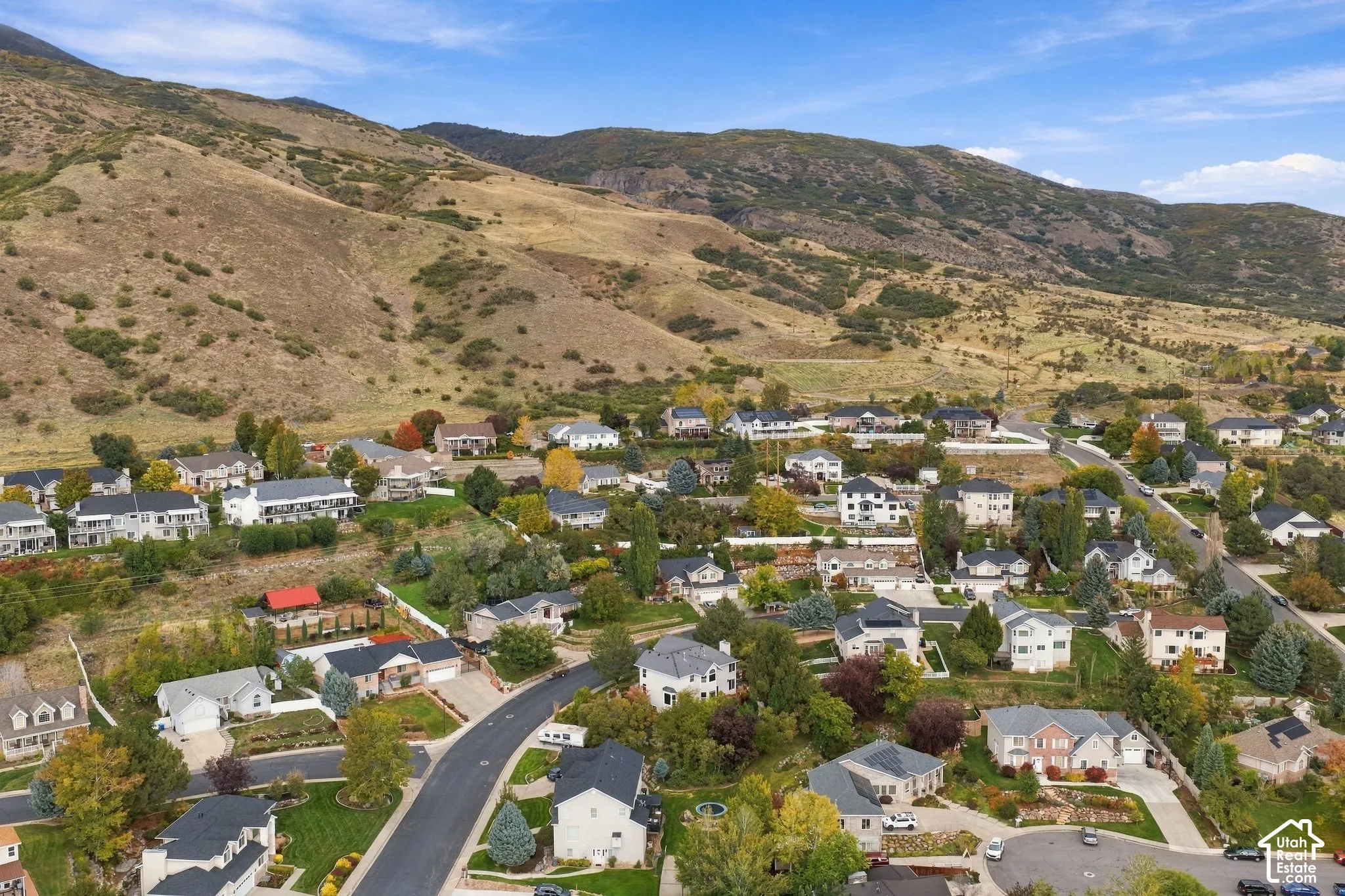 Aerial perspective of a hillside residential community featuring sloping terrain, established landscaping, mature trees, and mountainous topography