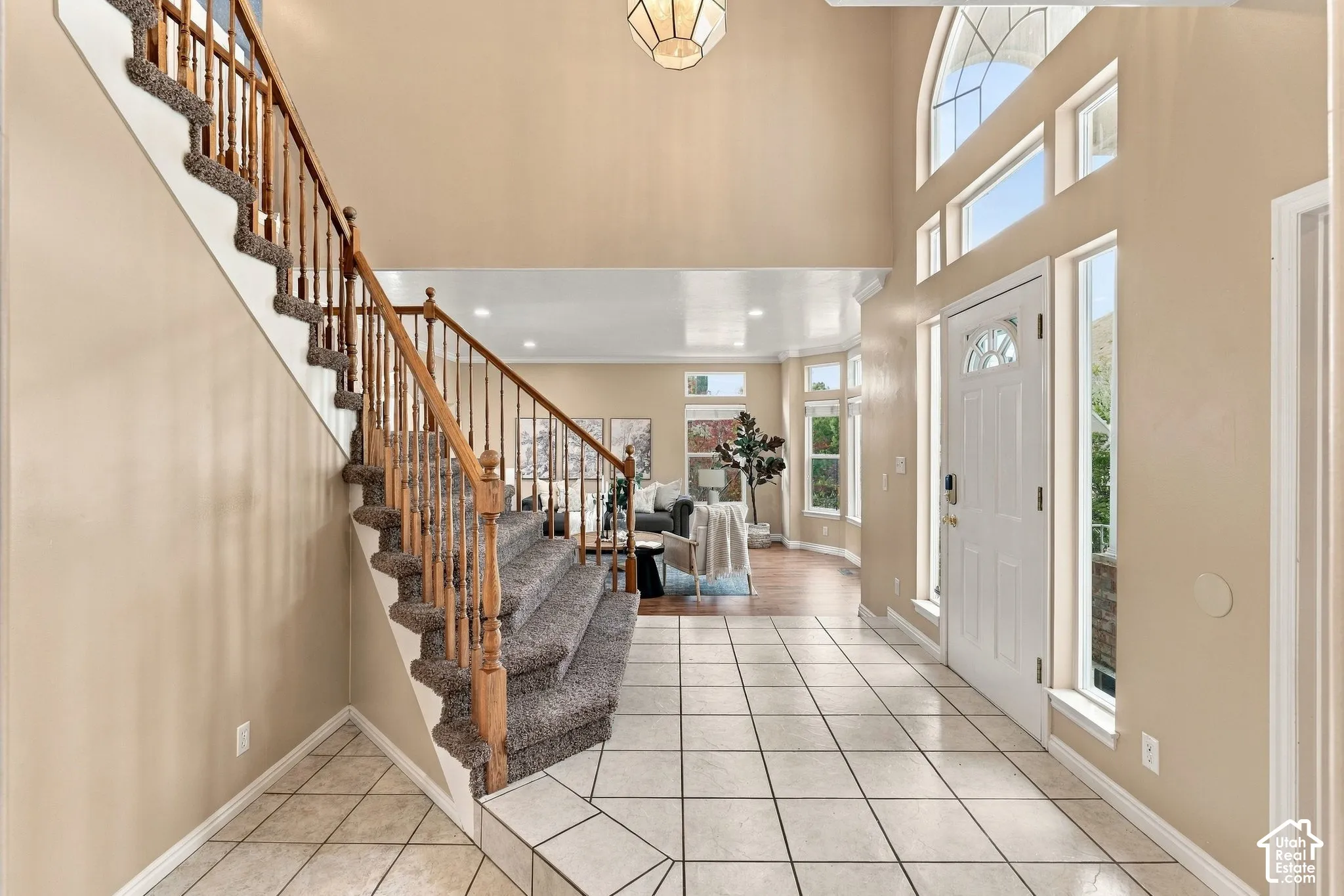Grand foyer featuring a vaulted ceiling, tile flooring, staircase with wood balusters, arched window, and a geometric pendant light fixture