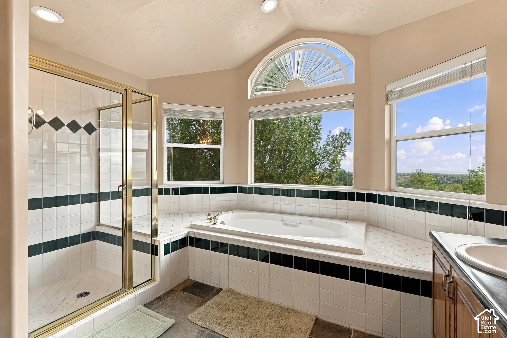Ensuite bathroom featuring a recessed soaking tub, glass-enclosed shower, vaulted ceiling with integrated lighting, and multiple windows including an arched transom window