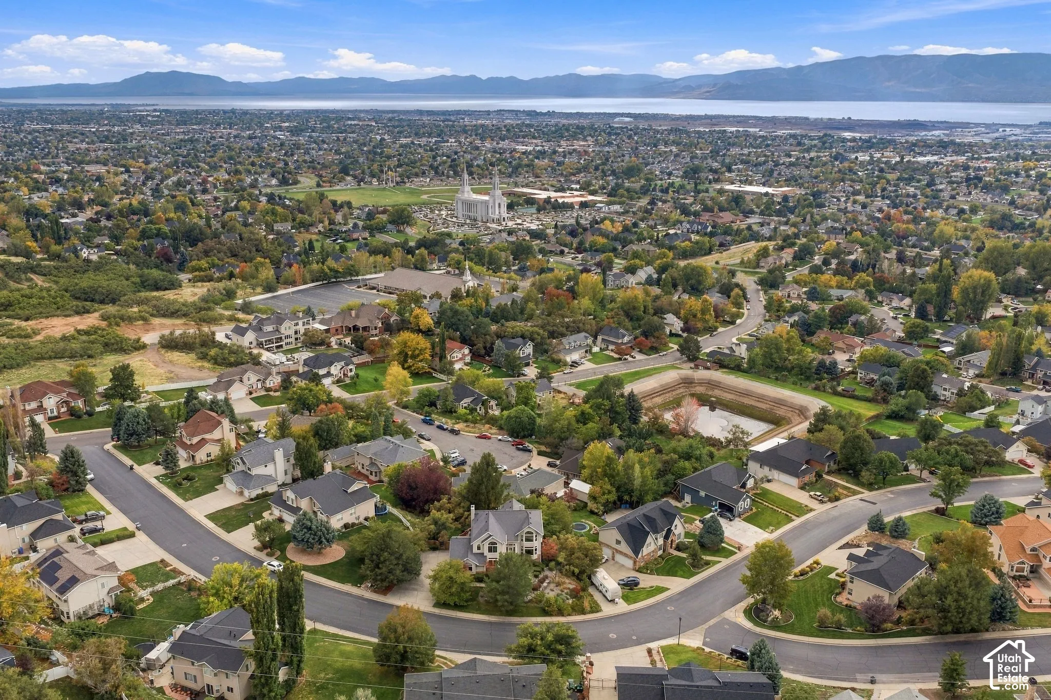 Aerial perspective of a suburban neighborhood featuring mature landscaping, paved roads, and a mountain backdrop