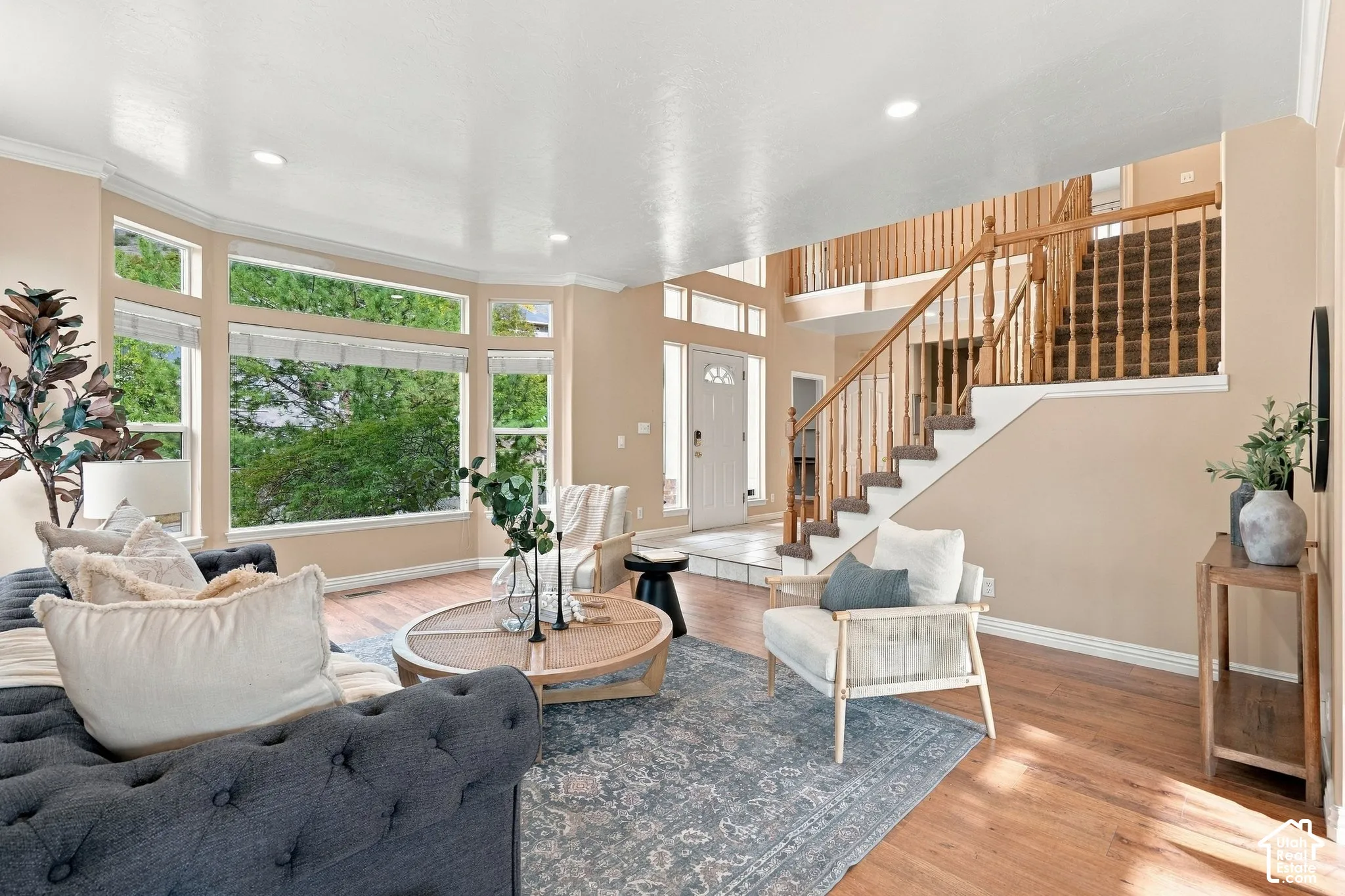 Open-concept interior featuring large bay windows, wood-finish flooring, recessed lighting, and a prominent staircase with a wood balustrade