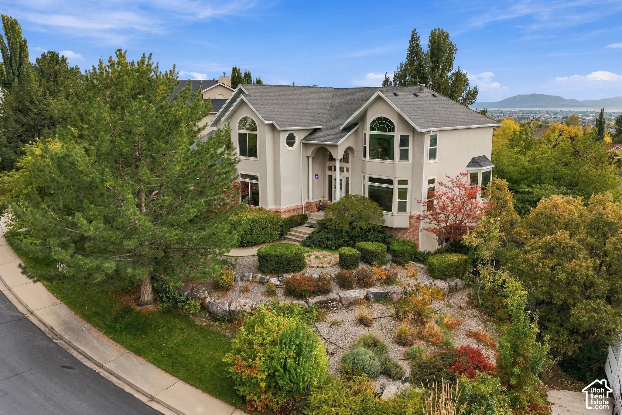 Two-story residence featuring a multi-gabled roofline, arched window detailing, stone retaining walls, tiered landscaping, and an attached multi-car garage