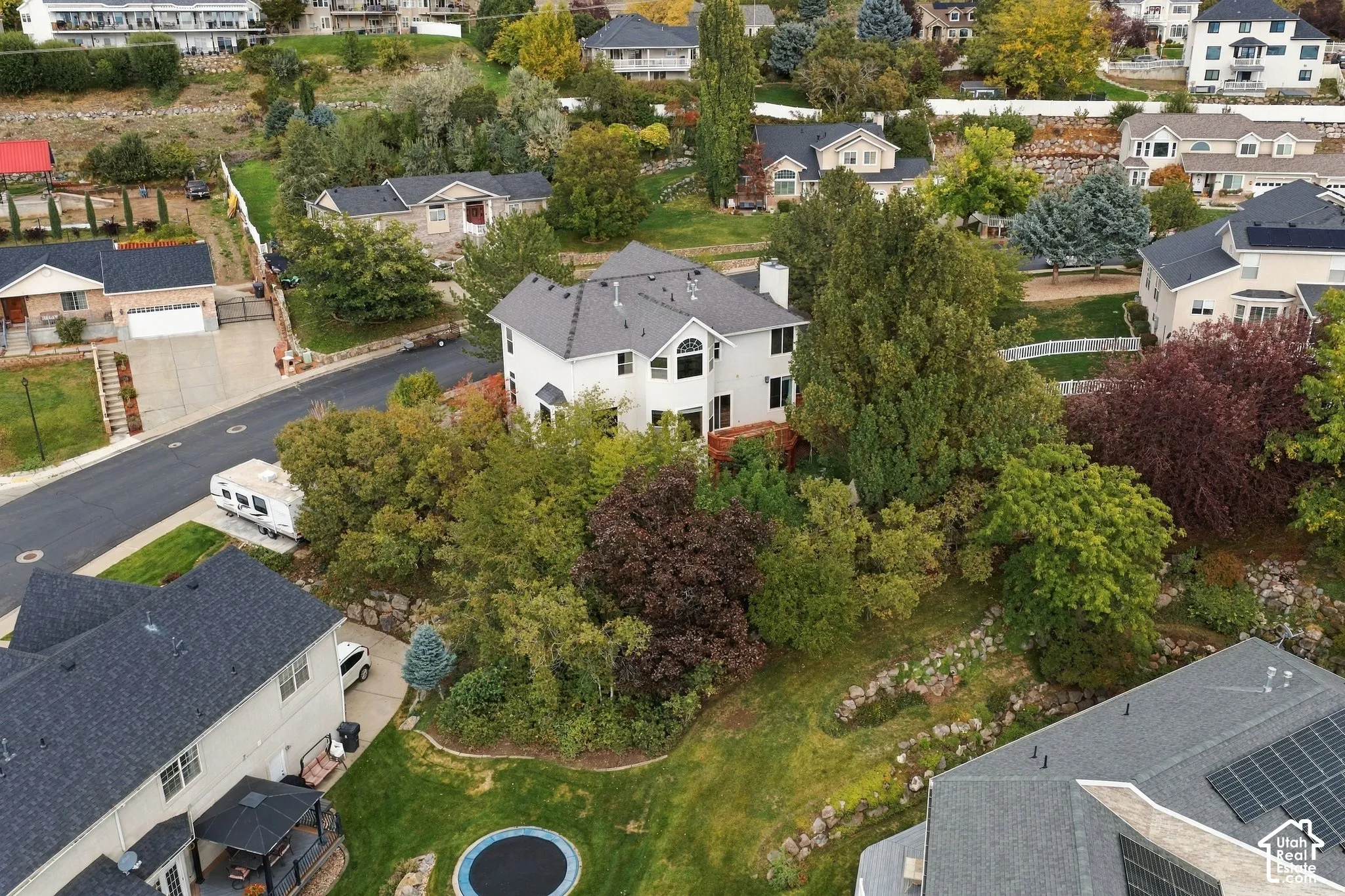 Multi-level residence featuring an exterior with arched window detailing, a chimney, and a mature tree canopy situated on a tiered lot with stone landscaping elements
