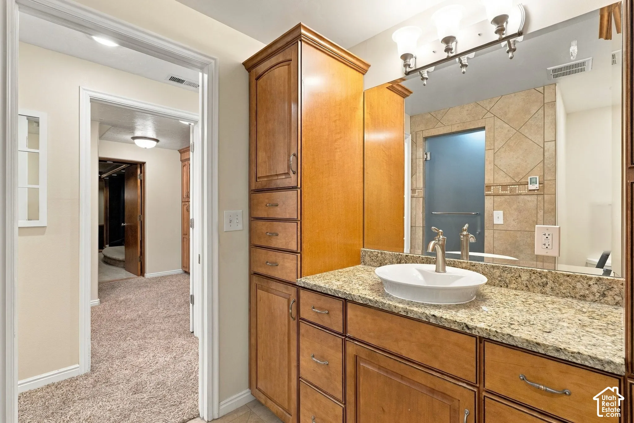 Bathroom vanity featuring wood cabinetry, stone-surface countertop, oval vessel sink, and an integrated full-height linen tower