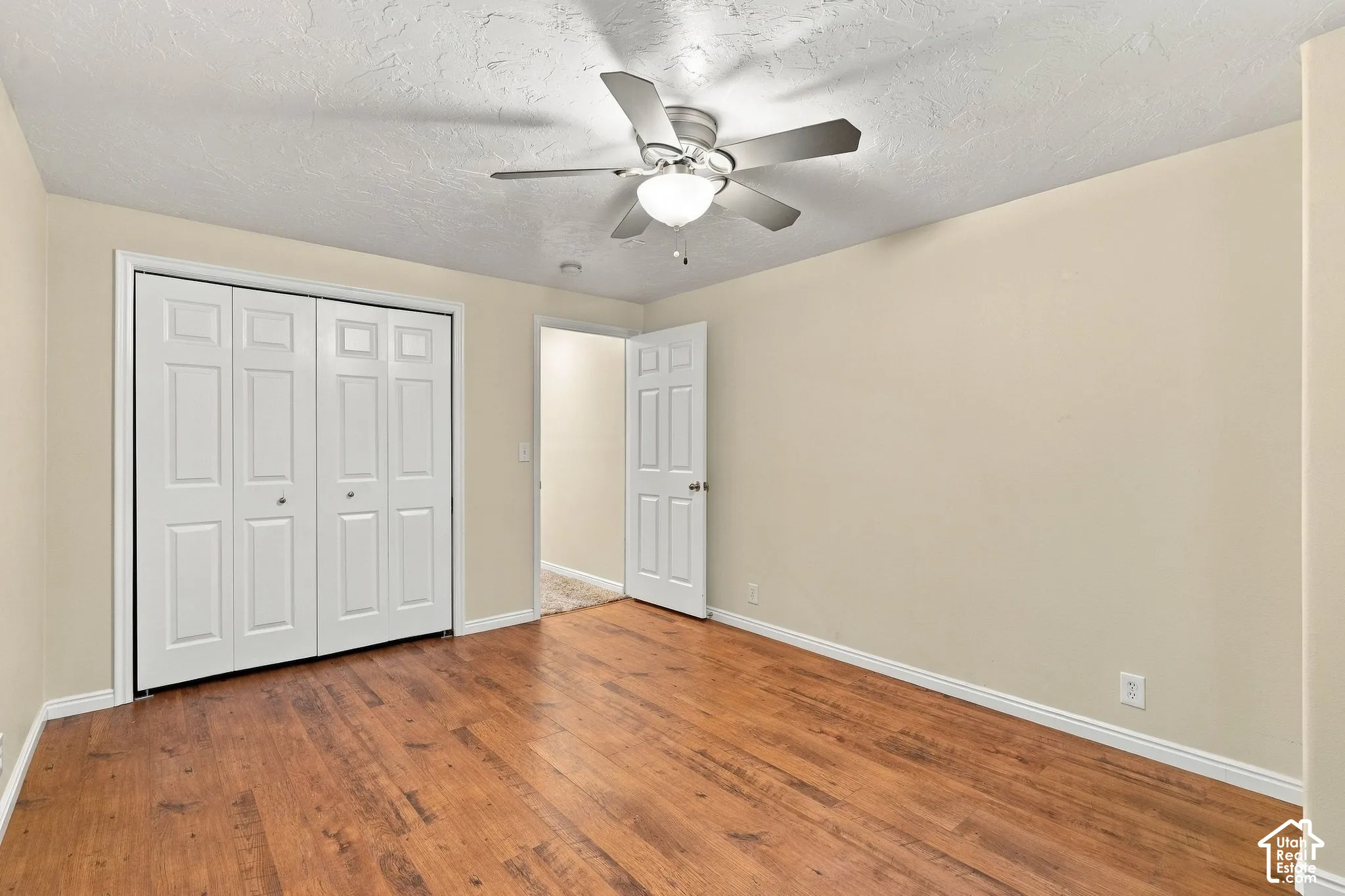 Room featuring wood-finish flooring, a ceiling fan with integrated lighting, and a bifold door closet