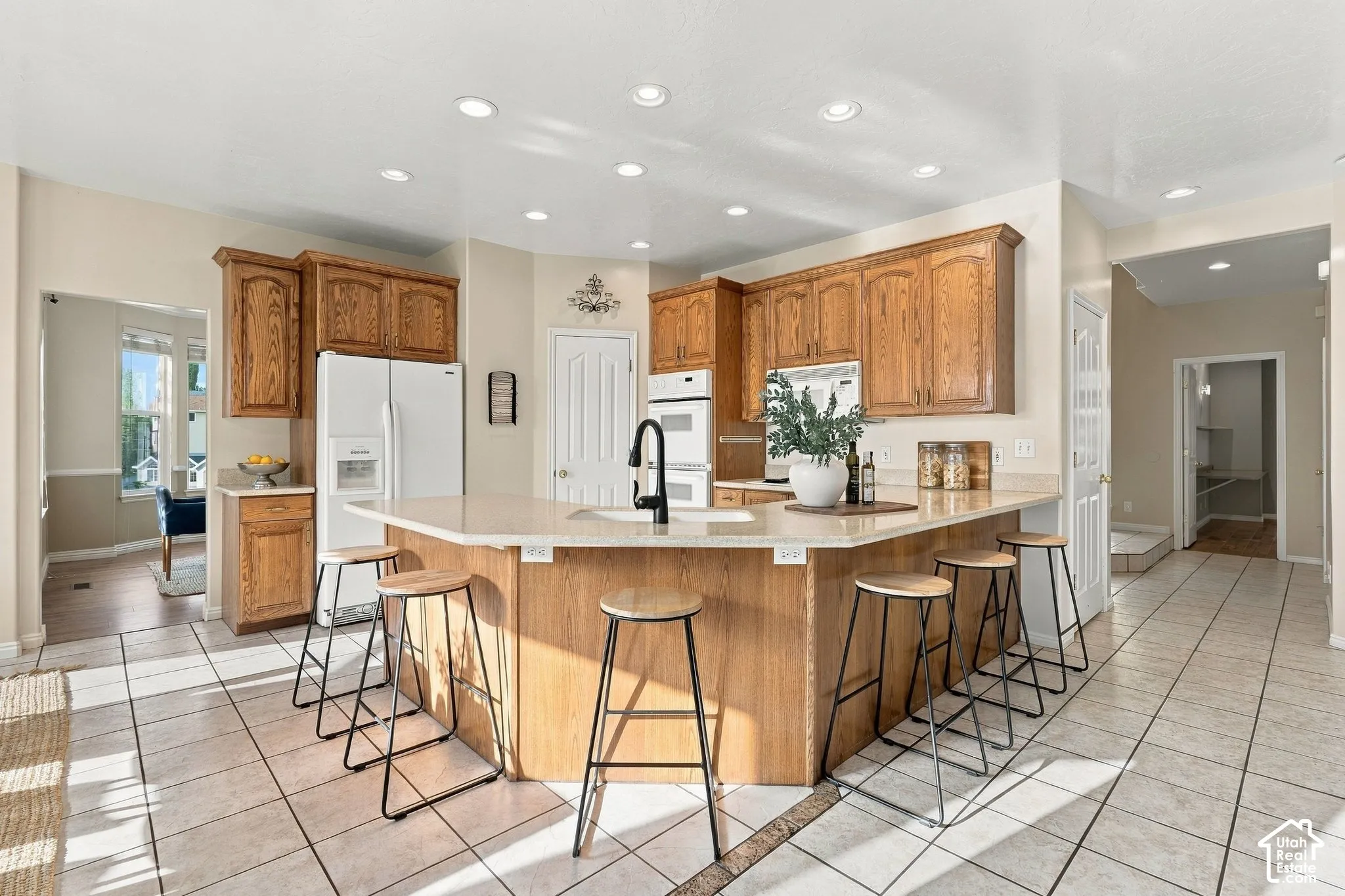 Kitchen featuring wood cabinetry, solid-surface countertops, a center island with a prep sink, recessed ceiling lighting, and tile flooring