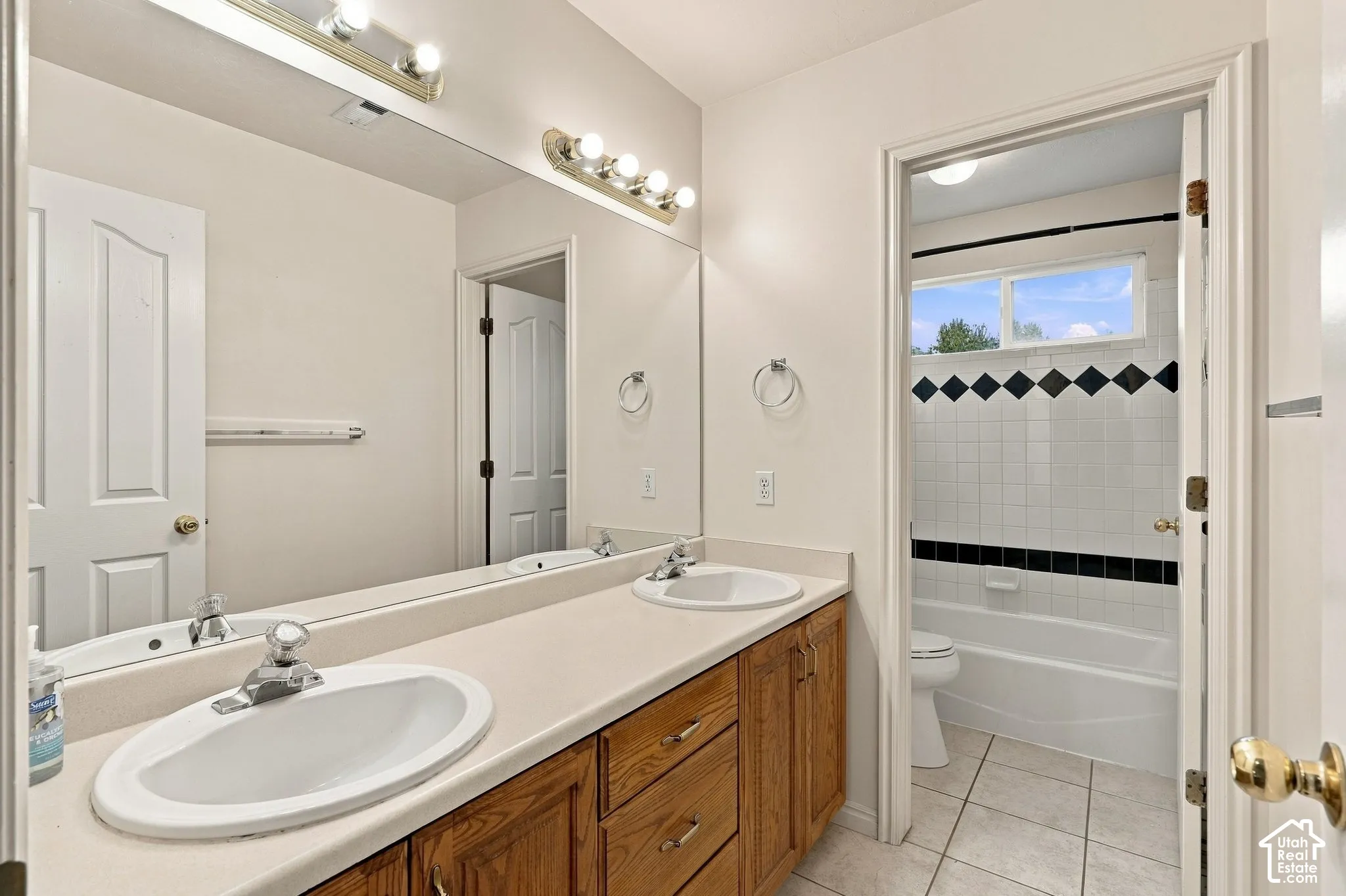 Double vanity featuring wood cabinetry, solid-surface countertops, recessed oval sinks, and a full-width wall mirror