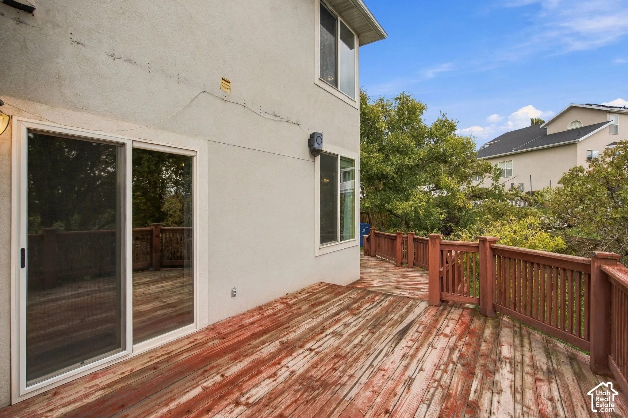 Stucco exterior featuring an expansive wood-plank deck with integrated railing, a sliding glass door, and exterior wall-mounted lighting