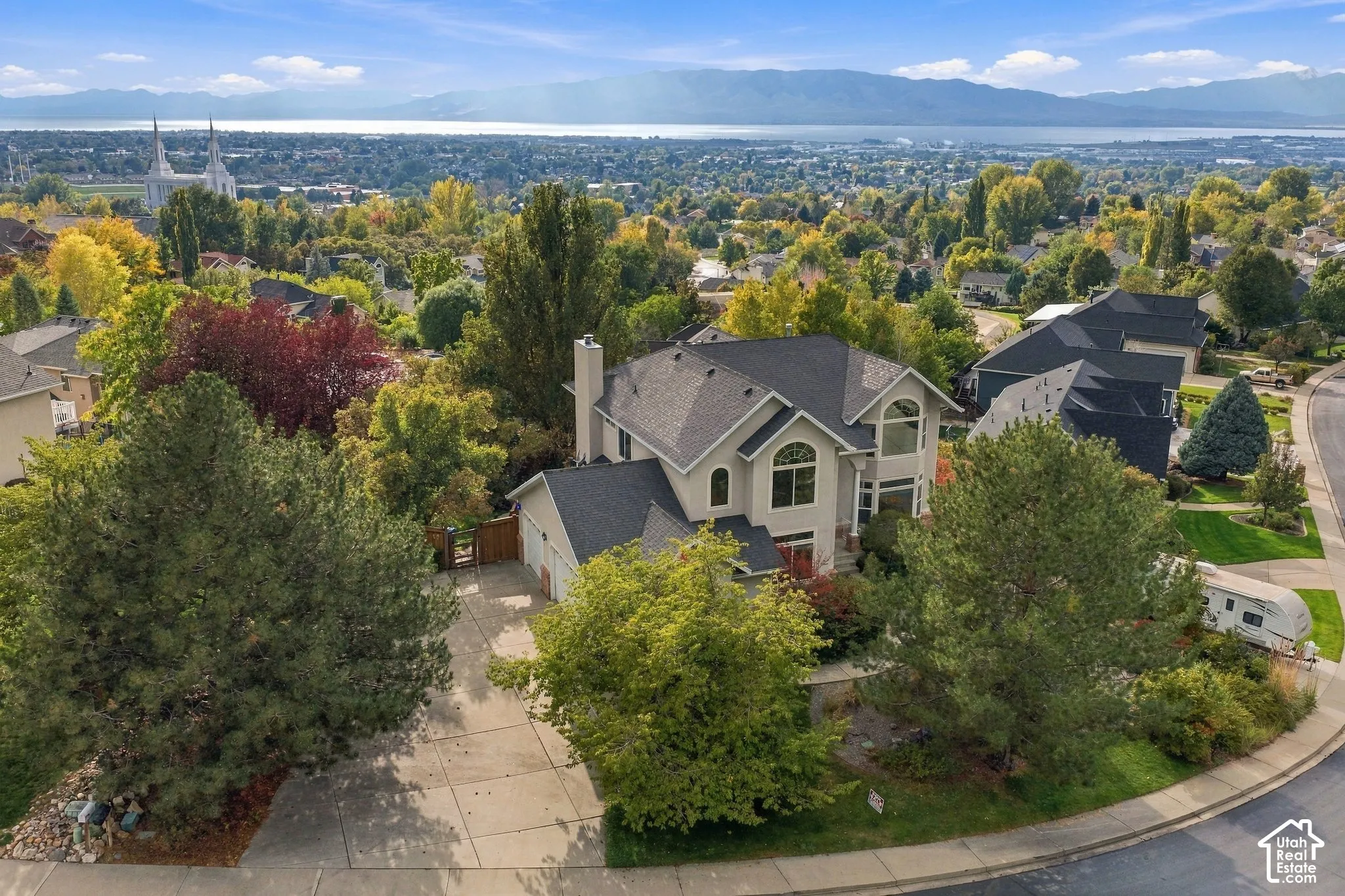 Multi-level residence featuring a pitched roof, exterior chimney, arched windows, concrete driveway, and mature landscaping
