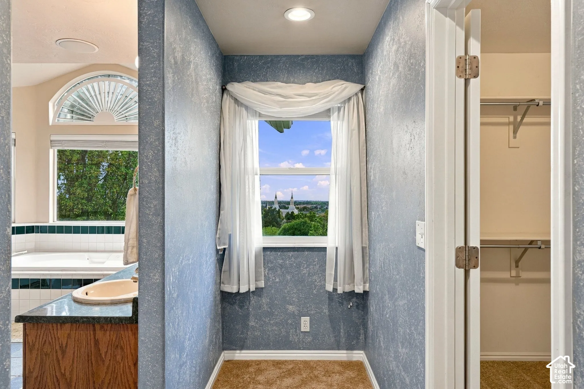 Built-in vanity featuring a dark stone countertop with integrated basin, recessed lighting, arched window with fanlight detailing, and walk-in closet with overhead shelving