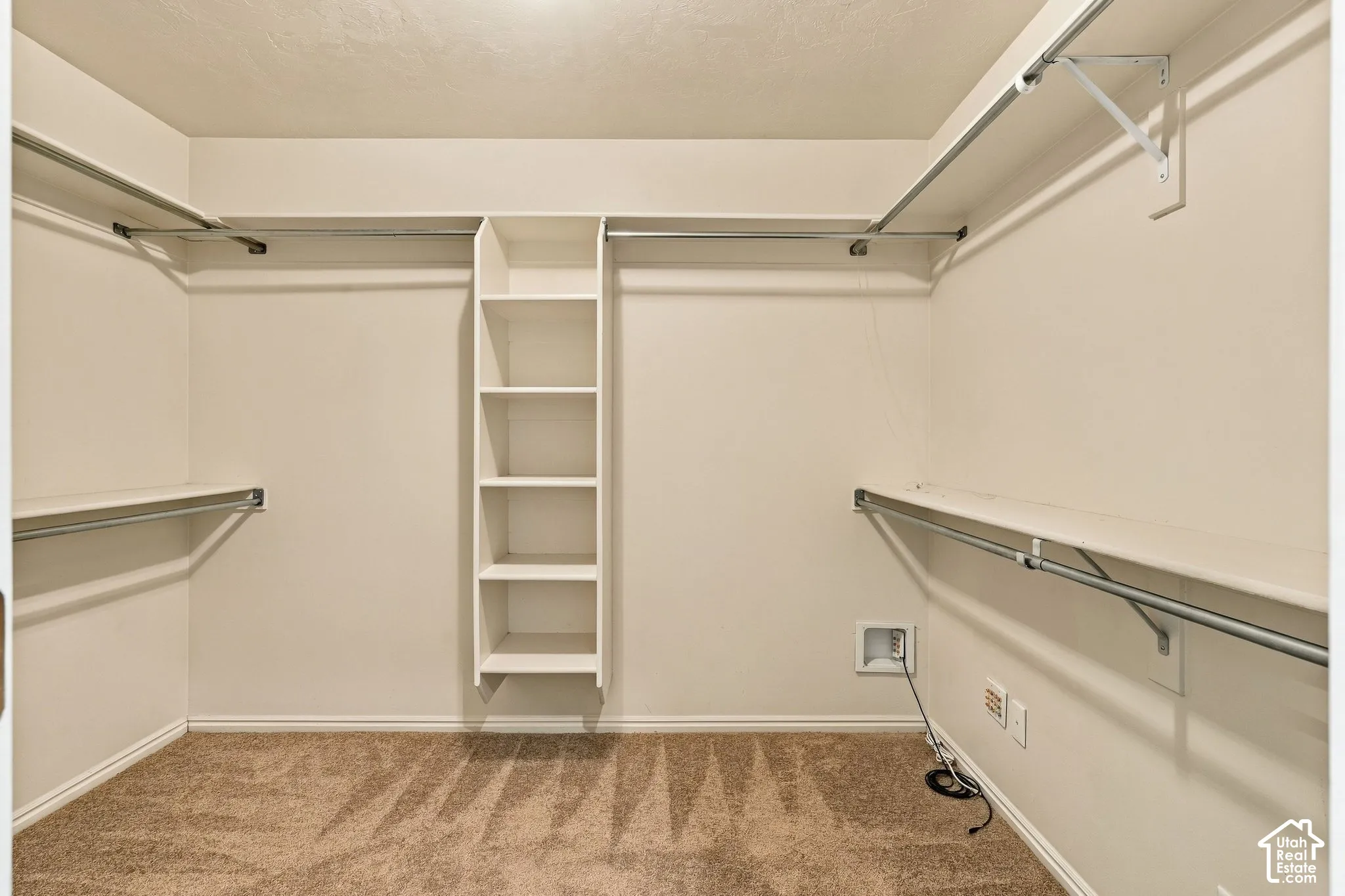 Walk-in closet featuring wall-to-wall carpet, built-in shelving tower, and tiered metal garment rods