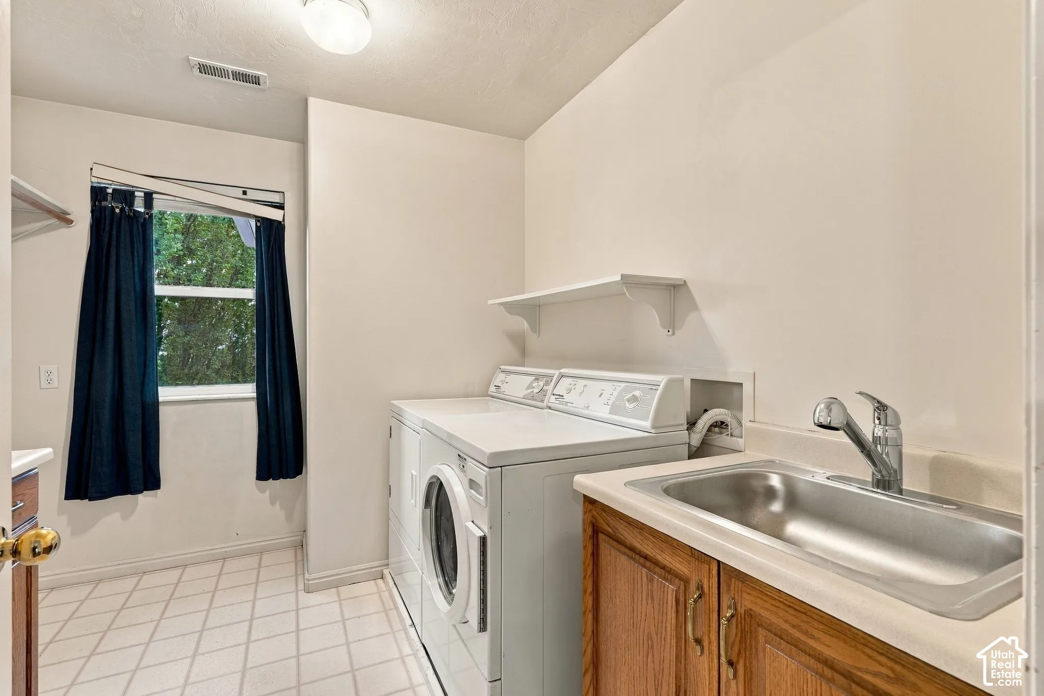 Utility room featuring tile flooring, a built-in wooden cabinet with an integrated stainless steel sink, a wall-mounted shelf, and natural lighting