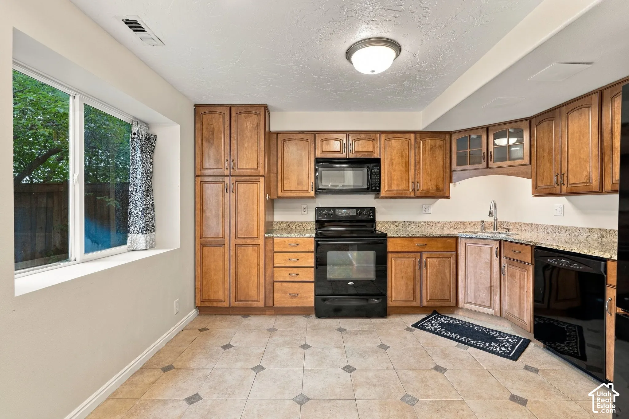 Kitchen featuring natural wood cabinetry, stone-finish countertops, black built-in appliances, large window, and tile flooring