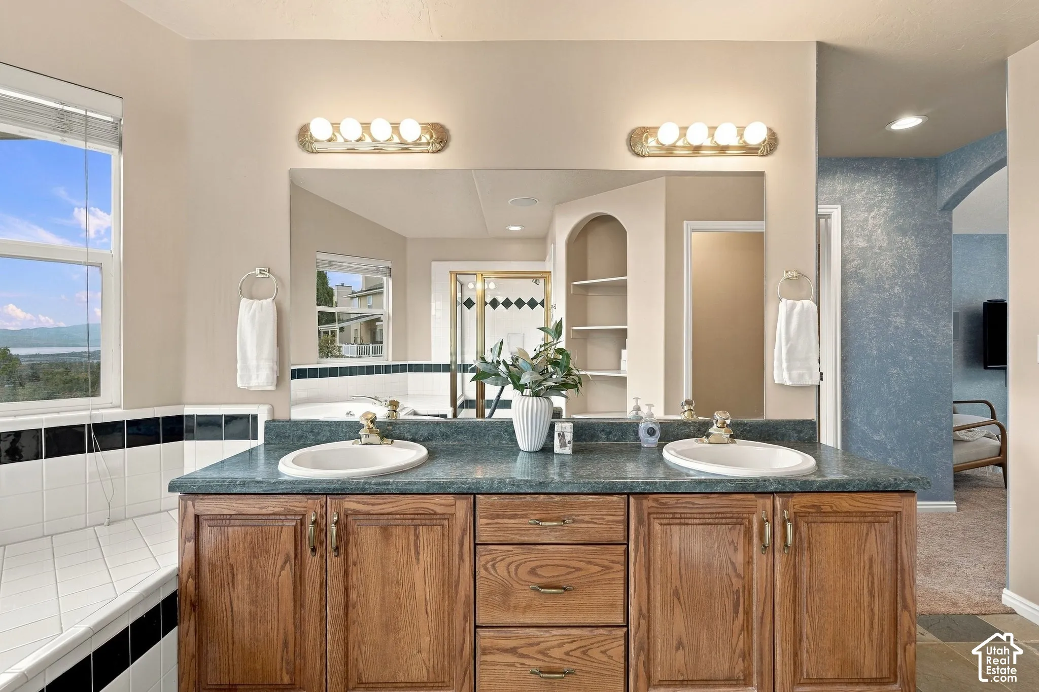 Double vanity featuring wood cabinetry, solid-surface countertops, recessed oval sinks, a large wall-mounted mirror, and dual multi-bulb lighting fixtures
