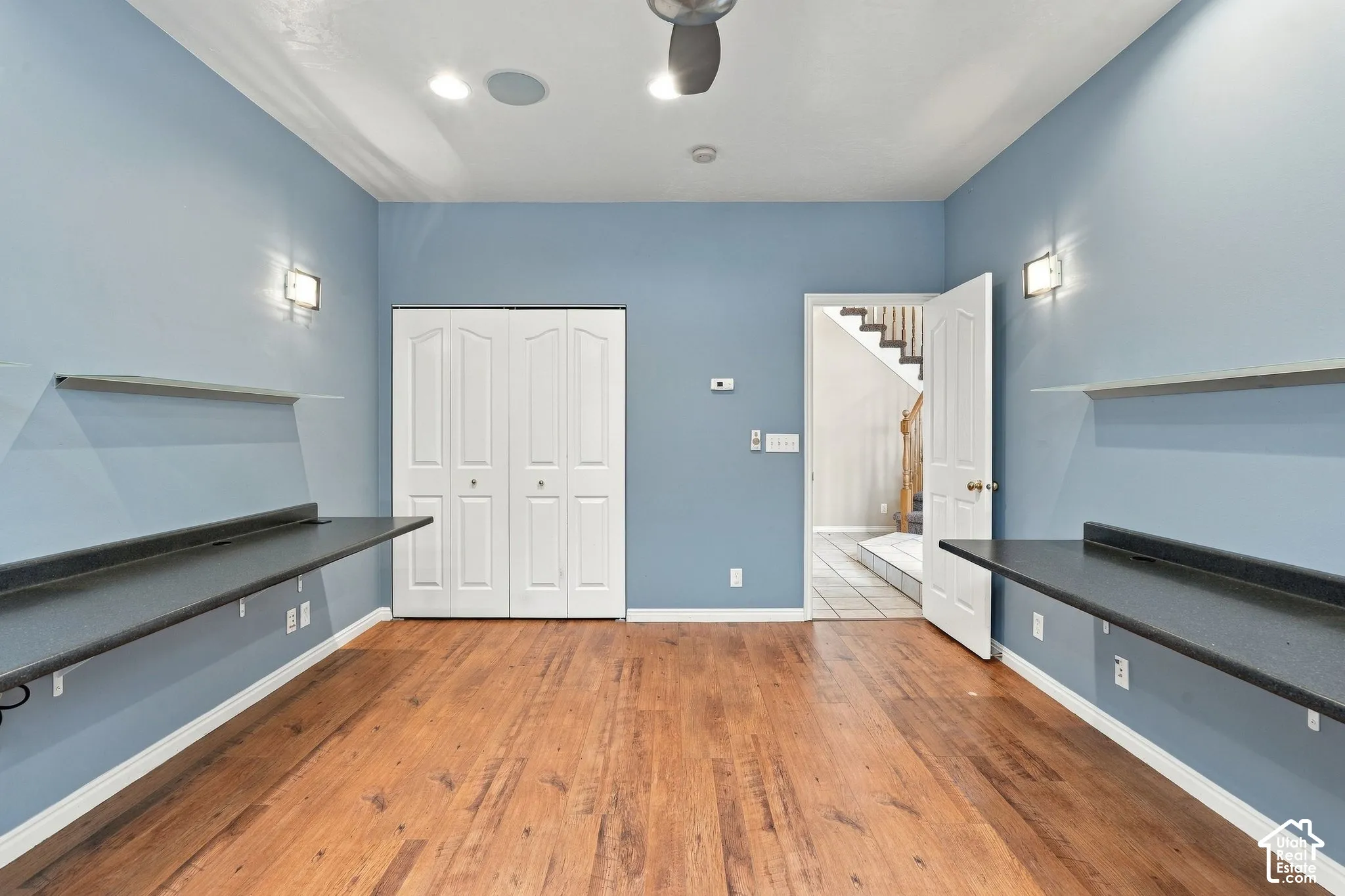 Wood-finish flooring, dual built-in counters with laminate surfaces, wall-mounted shelving, and folding closet doors