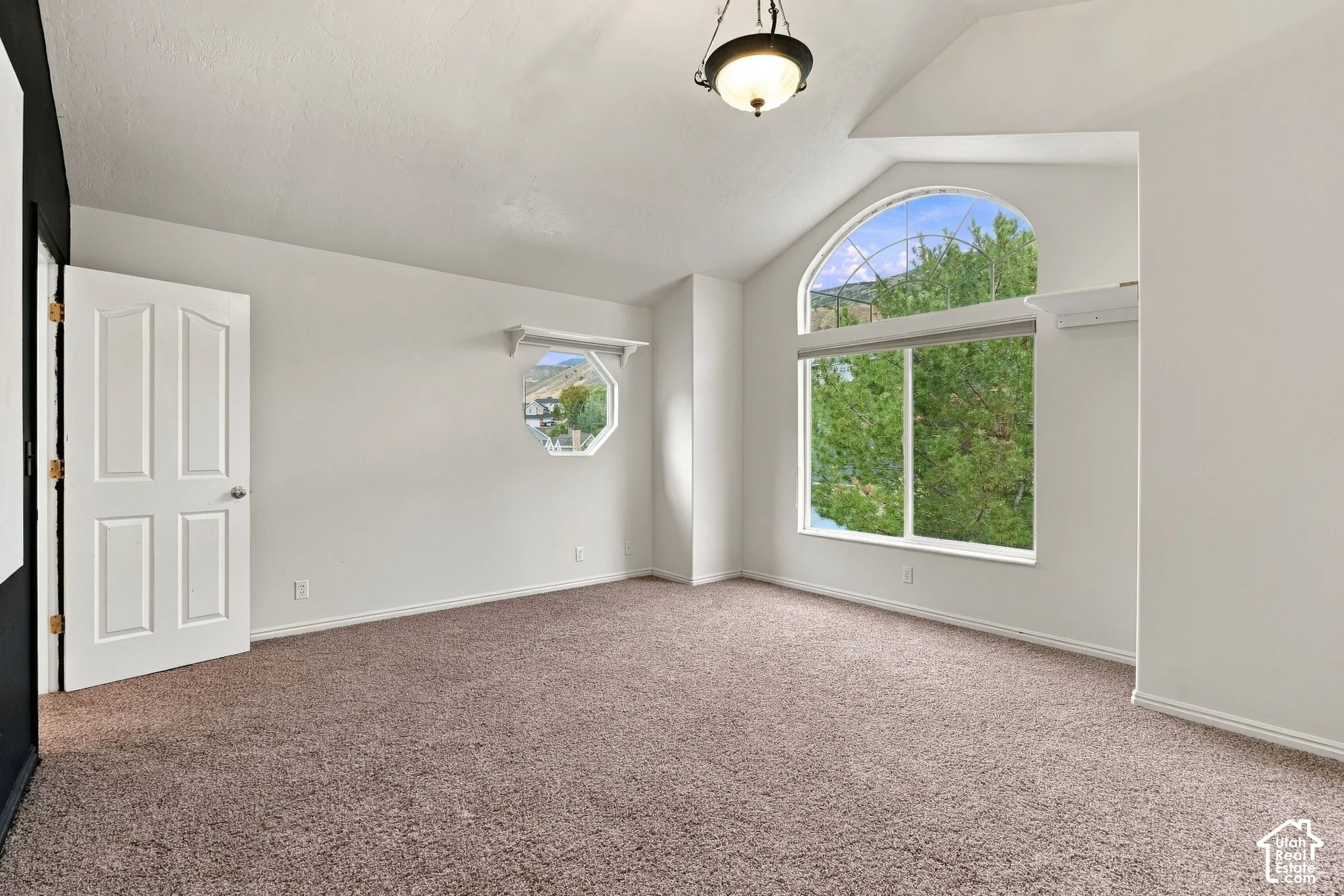 Vaulted ceilings, large arched window, octagonal accent window, carpeted flooring, and a central pendant light fixture